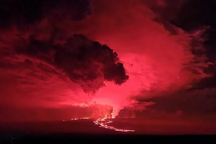 Nachtansicht eines ausbrechenden Vulkans mit rot glühender Lava und Rauch.